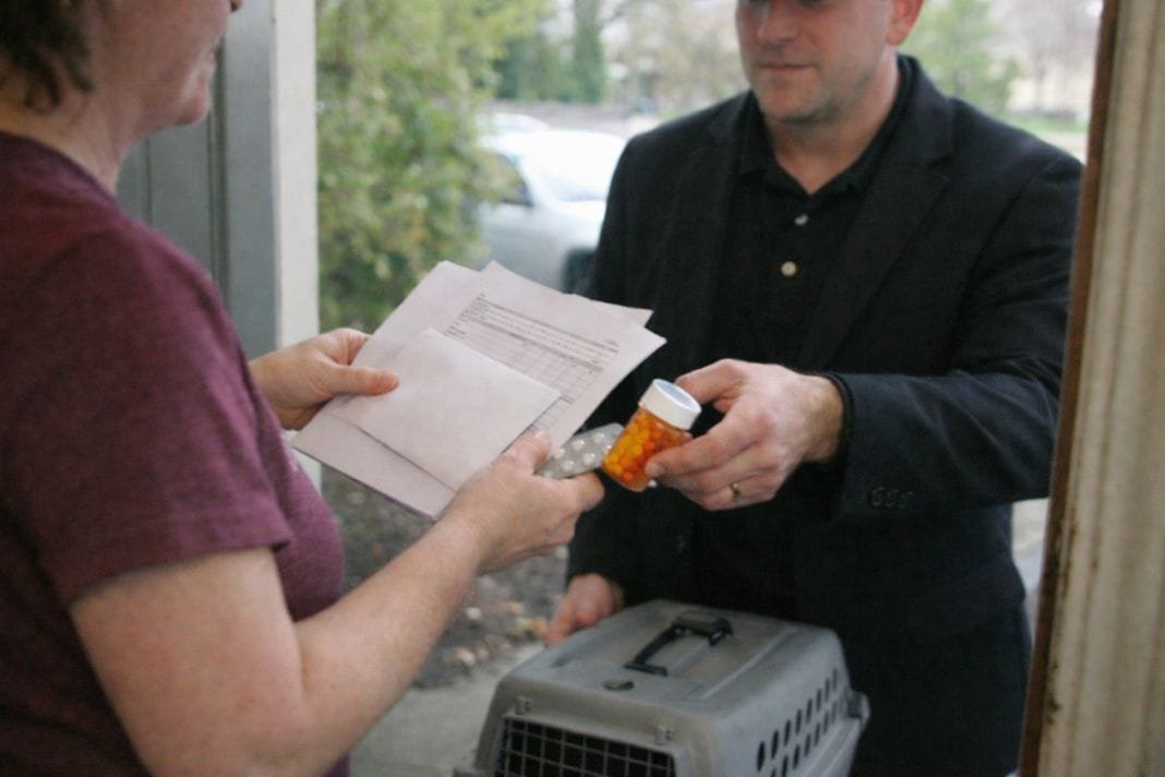 An illustrative image of a pet owner handing over medical documents and medication to a pet transport provider at their front door
