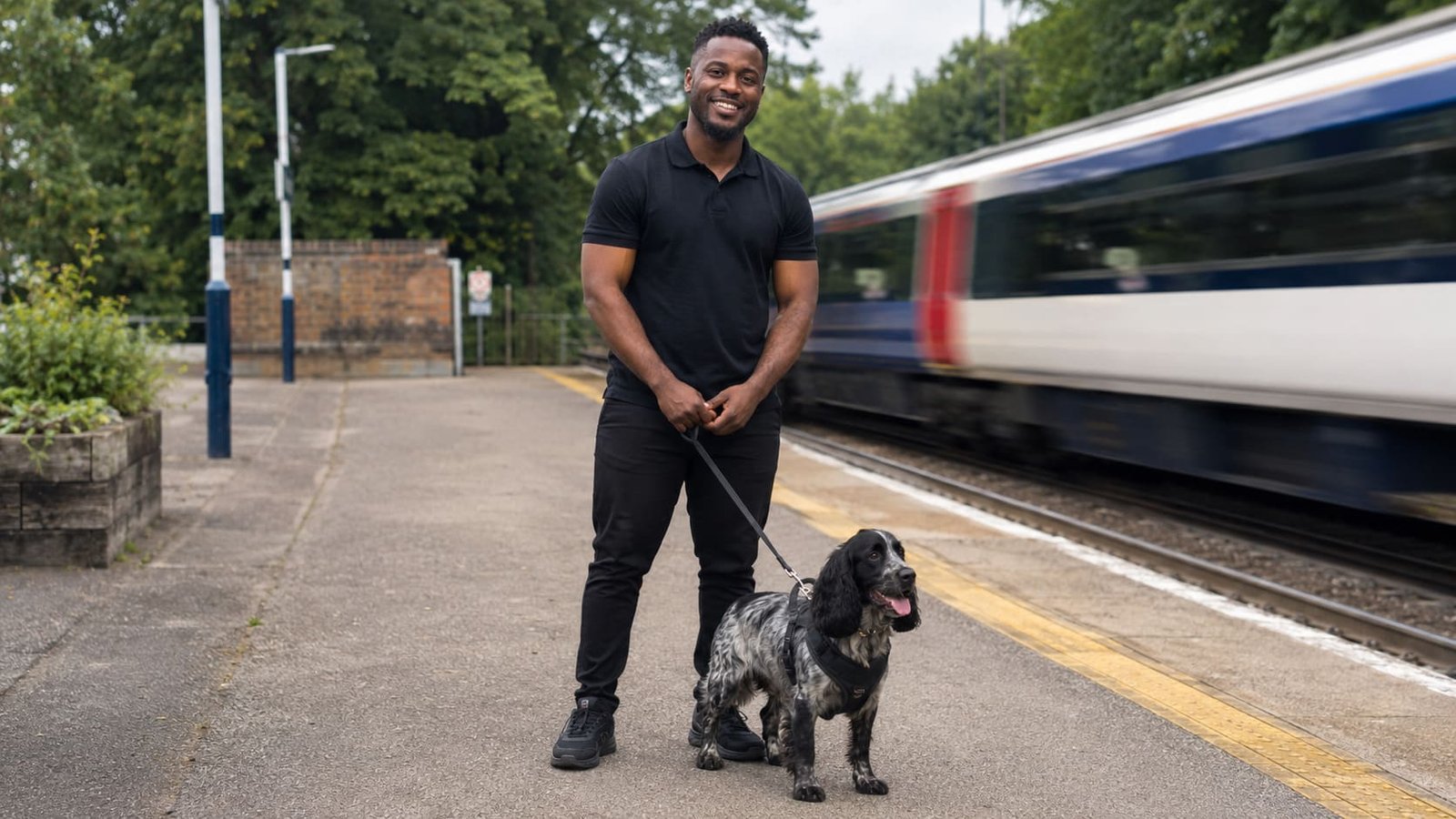 Handler waits with a harnessed dog beside a departing train. Handler waits with a harnessed dog beside a departing train.
