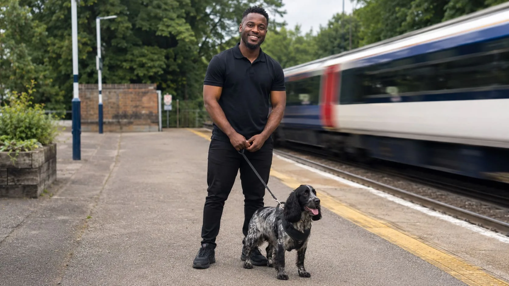 Handler waits with a harnessed dog beside a departing train.